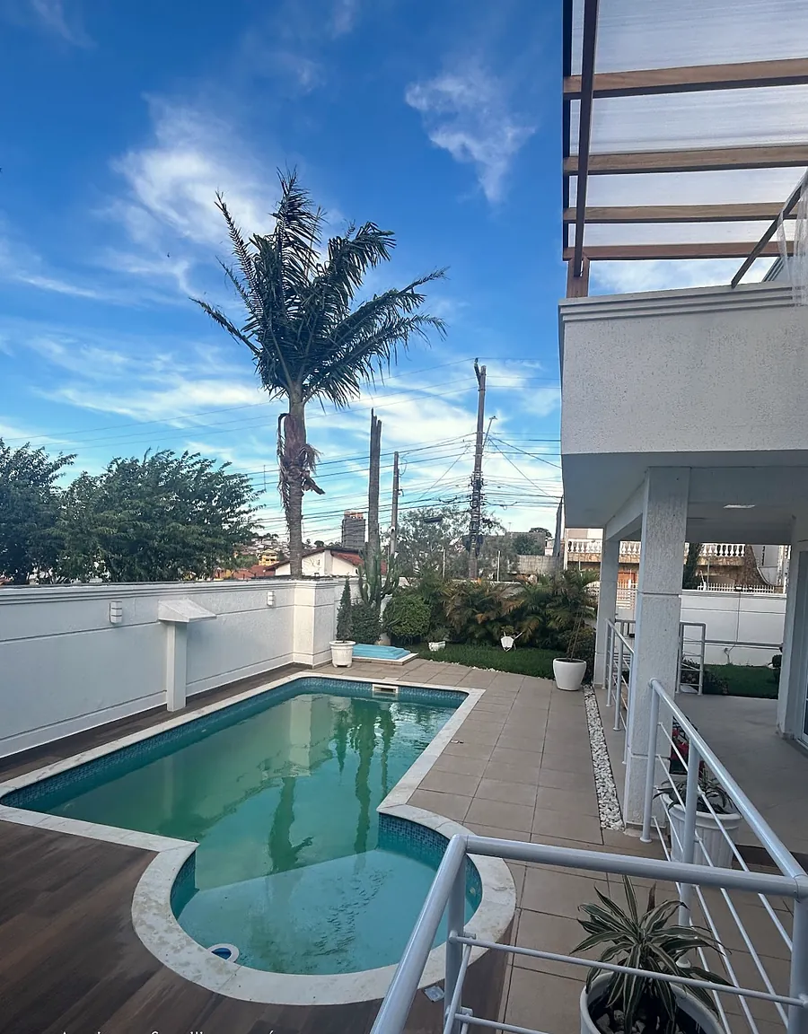 Piscina e jardim com palmeira, vistos da varanda do Villa Olívias, em dia de céu azul